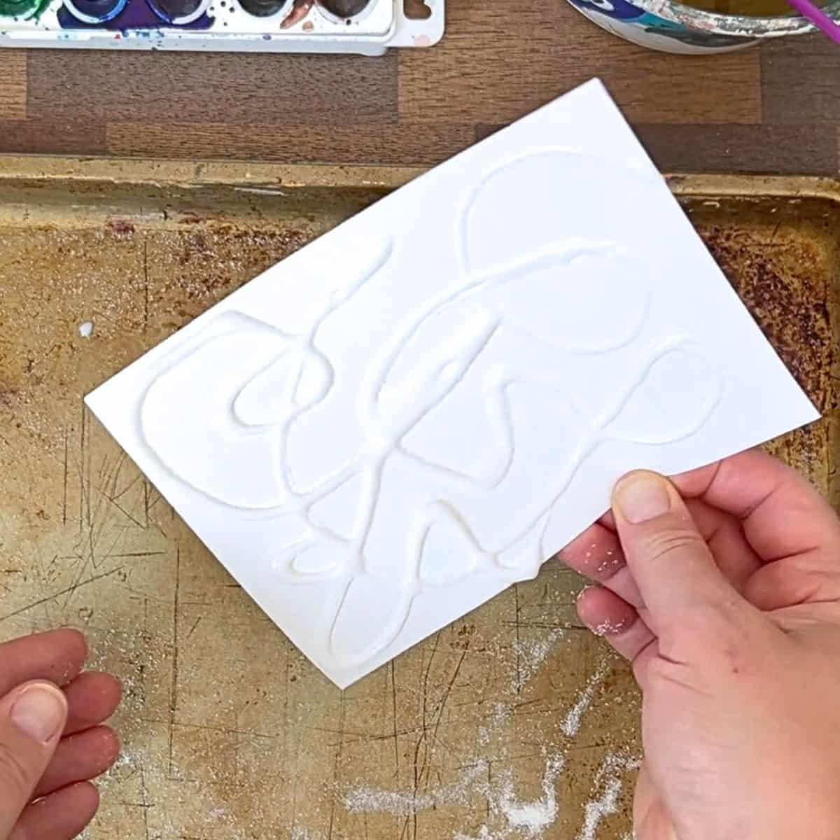 hand holding white paper with glue and salt lines on it.