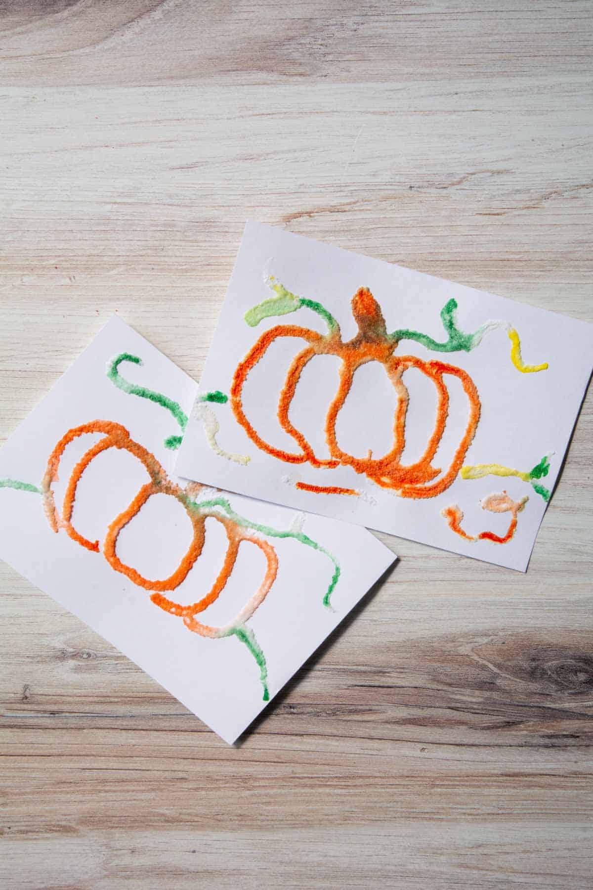 2 pumpkin salt paintings on white paper.