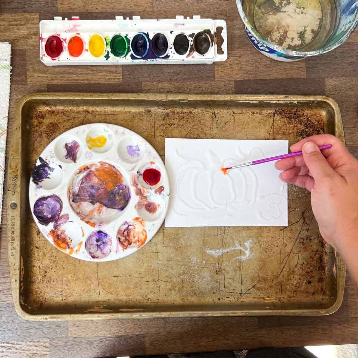 hand holding brush adding orange paint to pumpkin art.