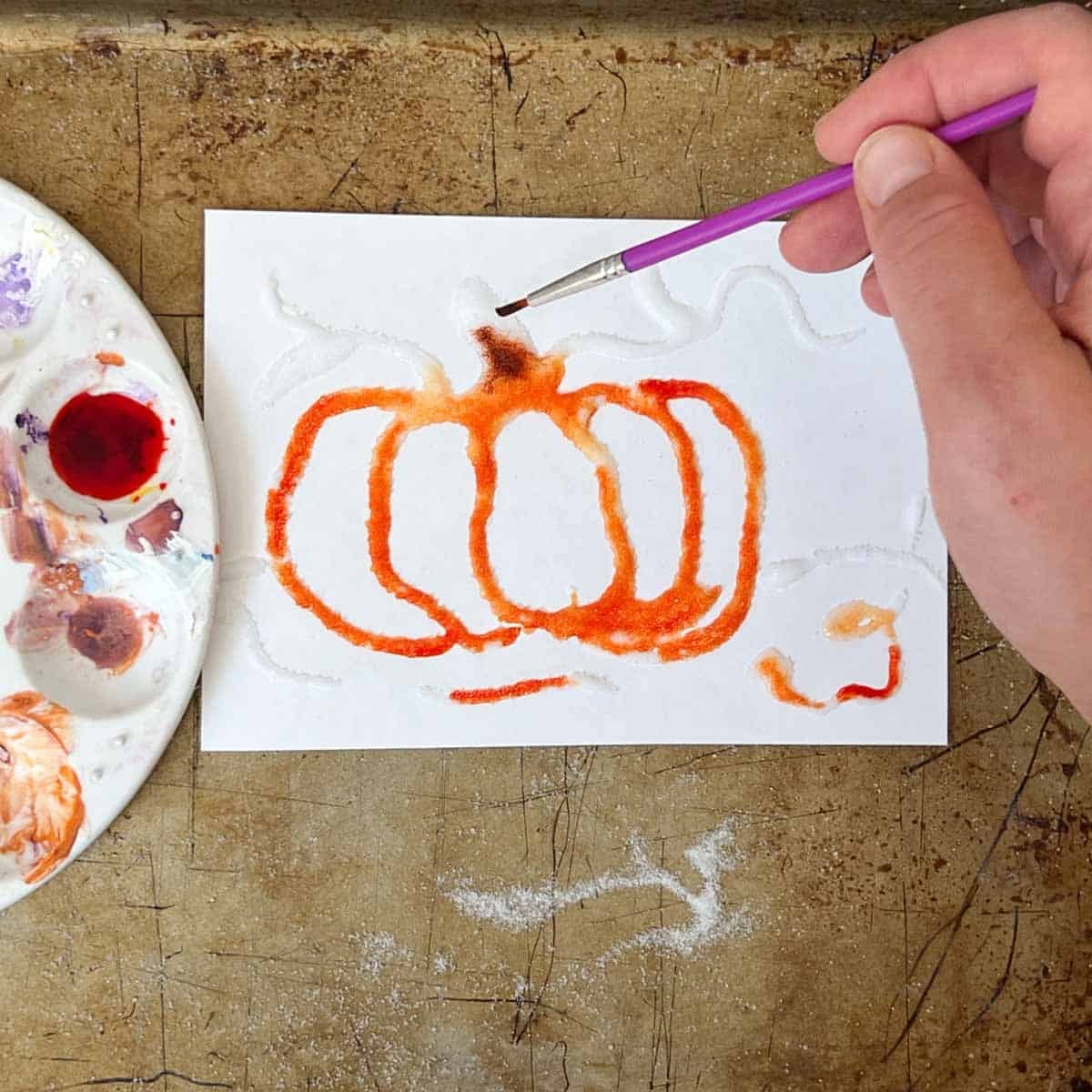 hand holding brush adding orange paint to pumpkin art.