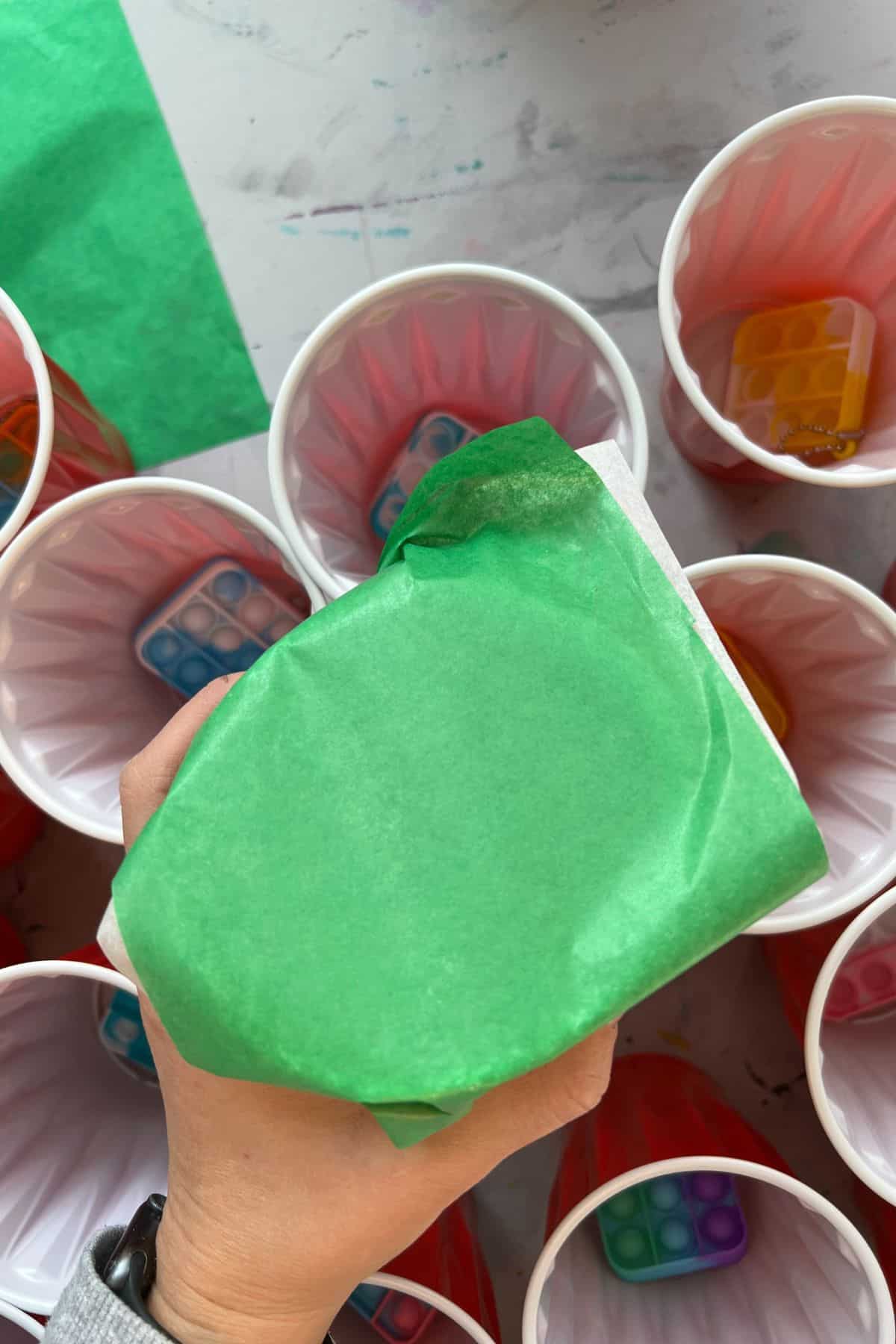 hand holding tissue paper over red cups with prizes in them.