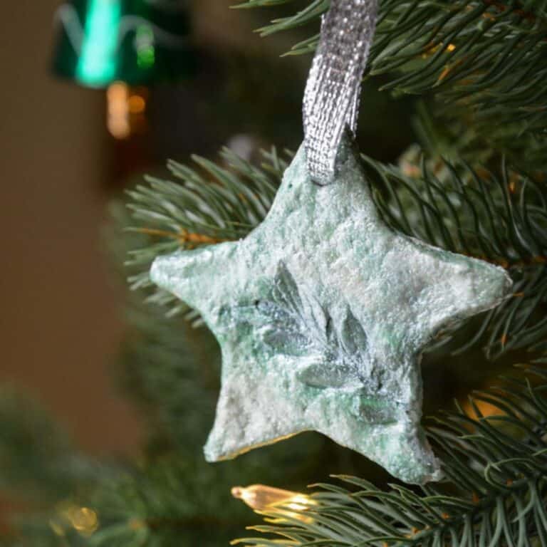 green salt dough star ornament with leaf design hanging on a Christmas tree.