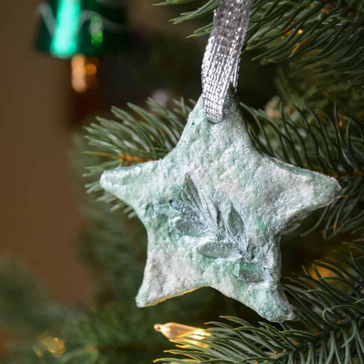 green salt dough star ornament with leaf design hanging on a Christmas tree.