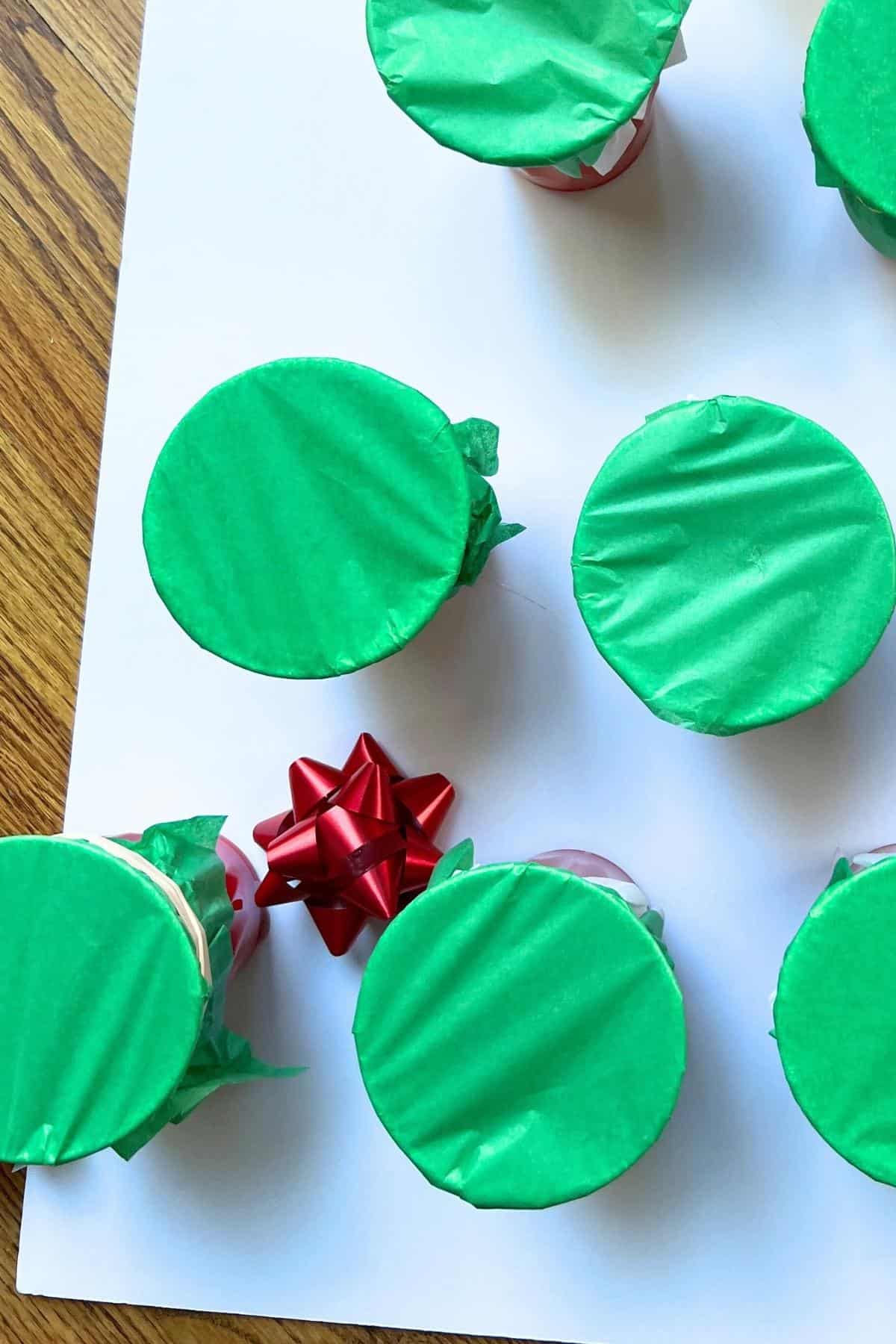 plastic bow on white foam core with green tissue paper covered cups.