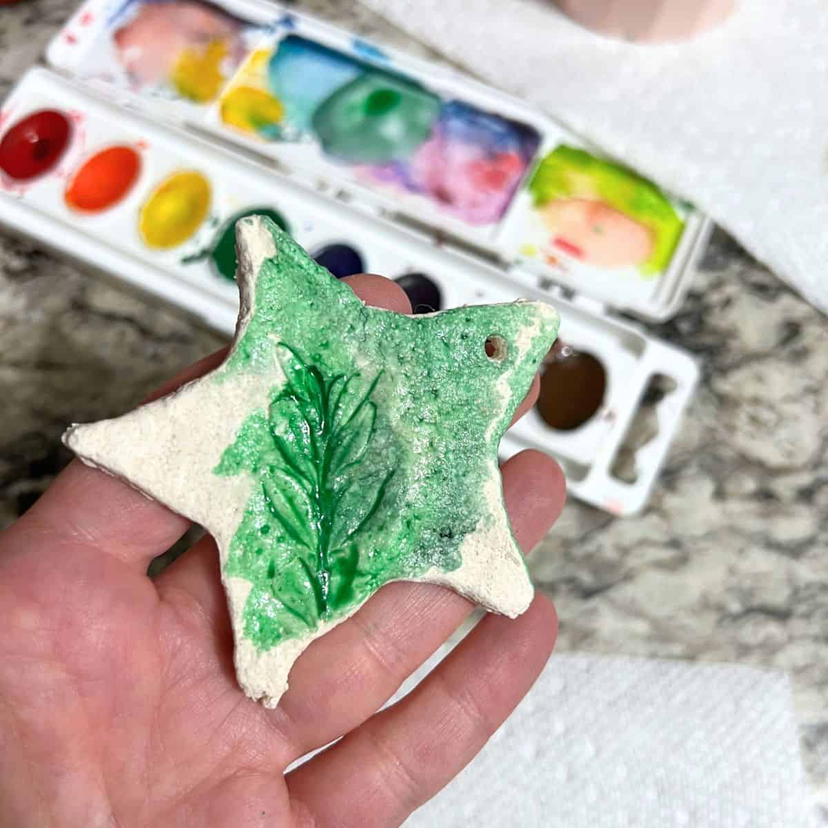 hand holding salt dough star with wet green paint on it.