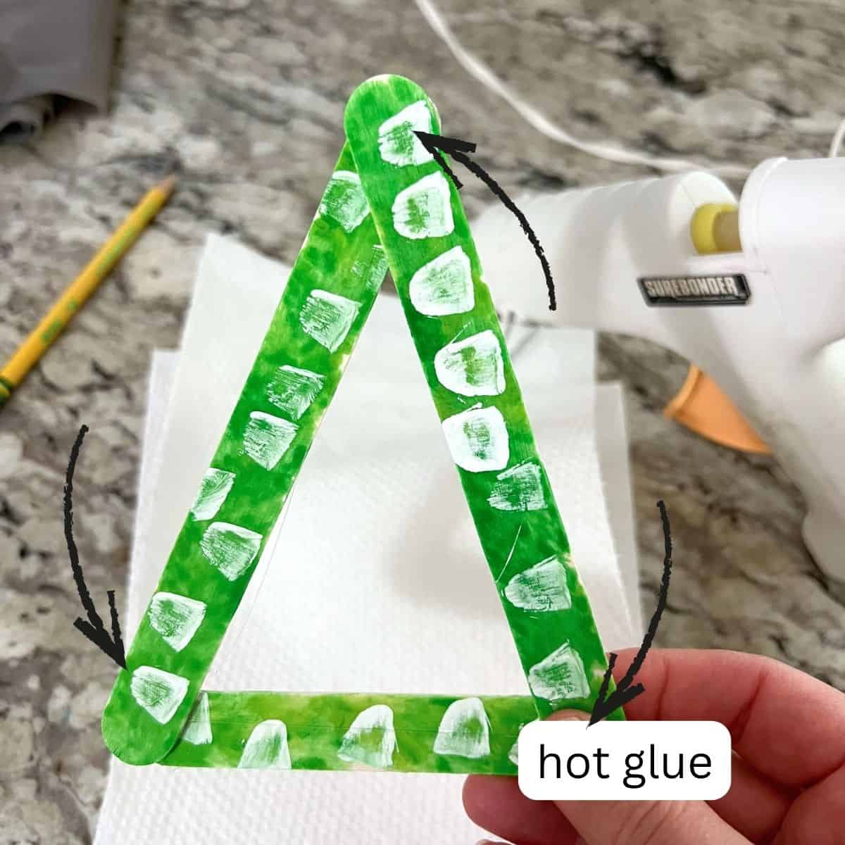 hand holding glue craft sticks in Christmas tree shape.