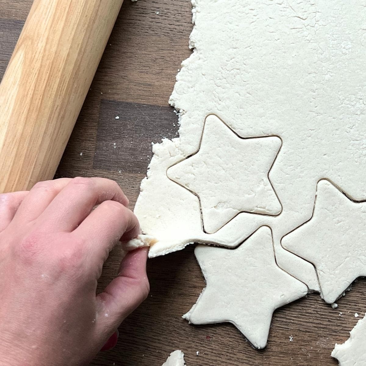 hand pulling away extra salt dough around cut out stars.