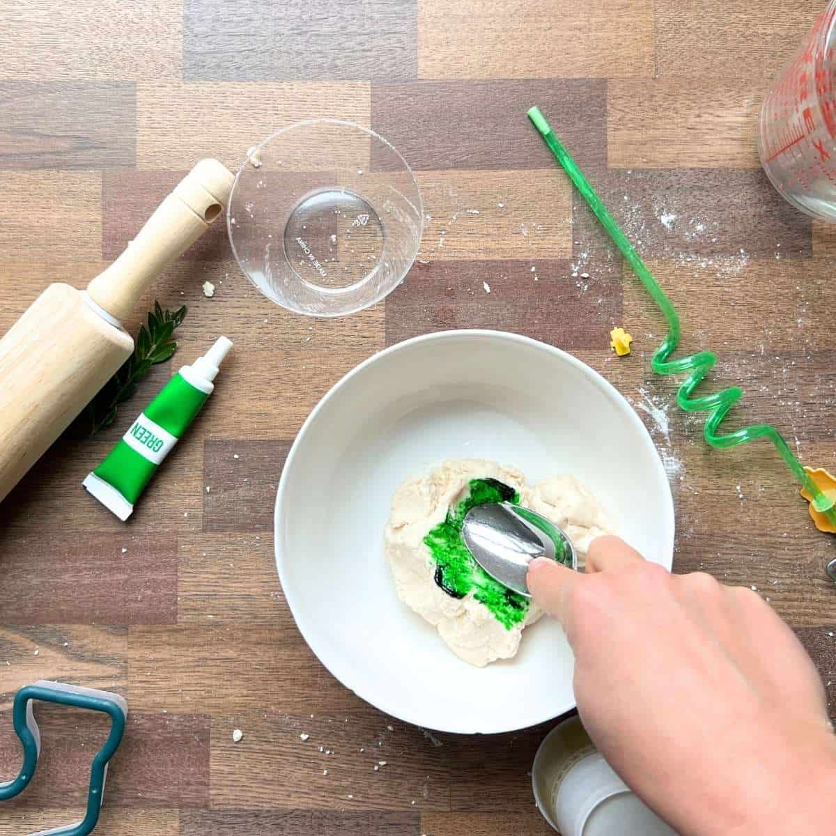 hand holding spoon to mix food coloring into salt dough.