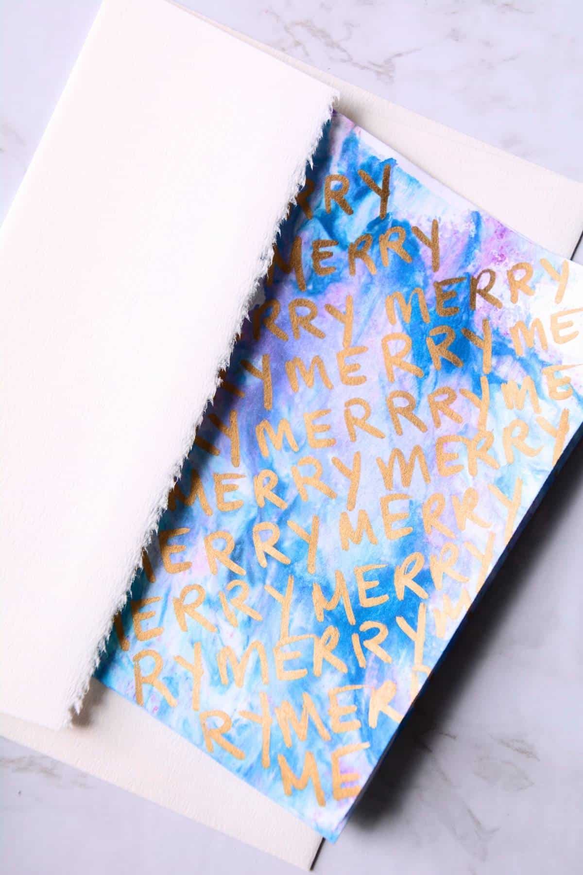 blue and purple design with word Merry repeated in gold marker on a card.