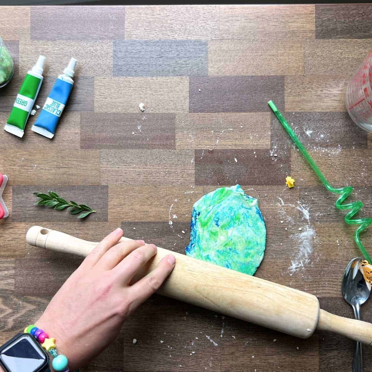 hand using rolling pin to make flat colored dough on table.