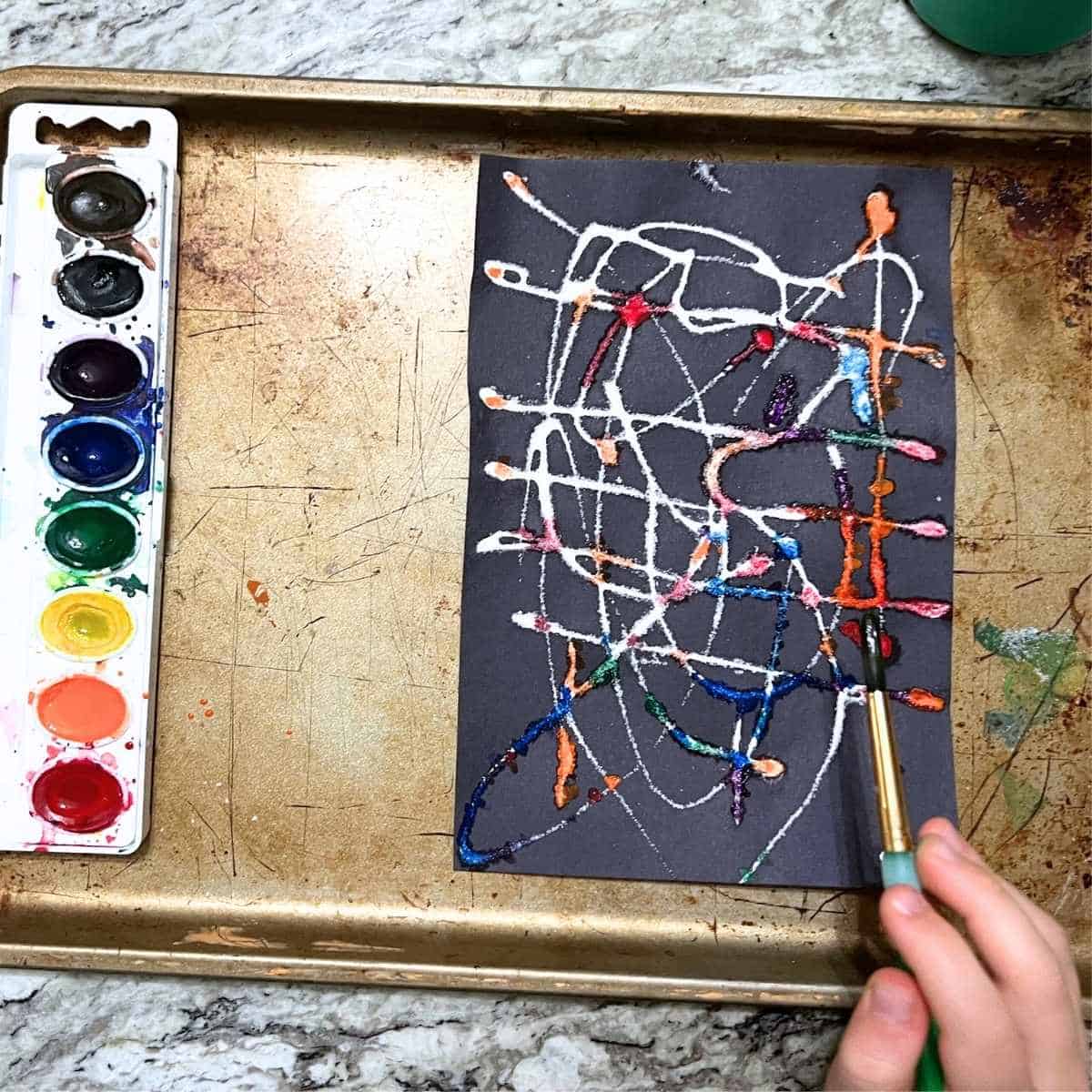child's hand adding watercolor to salt painting.