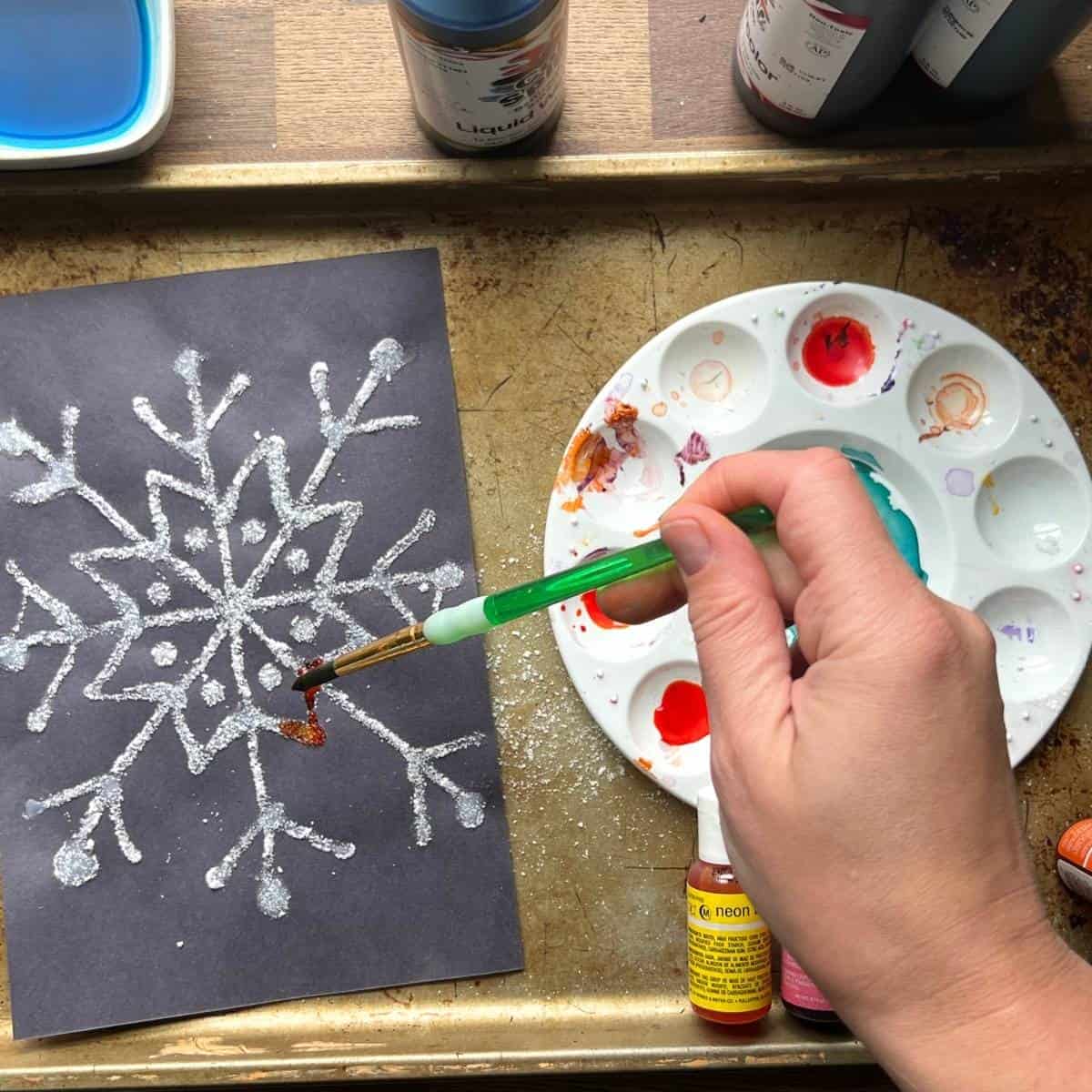 hand holding brush and adding color to raised salt snowflake painting.