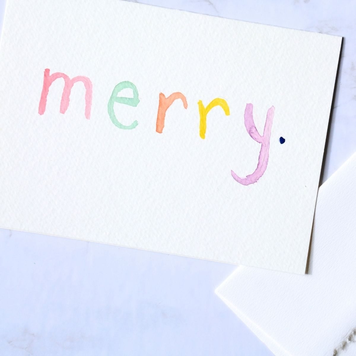 word merry painted with watercolor paint on a card.