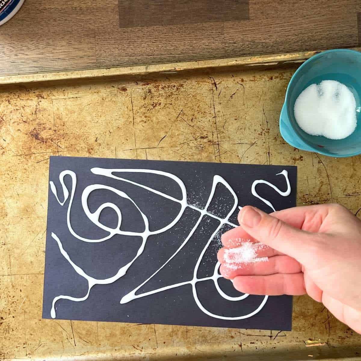 hand sprinkling salt on glue lines on black paper.