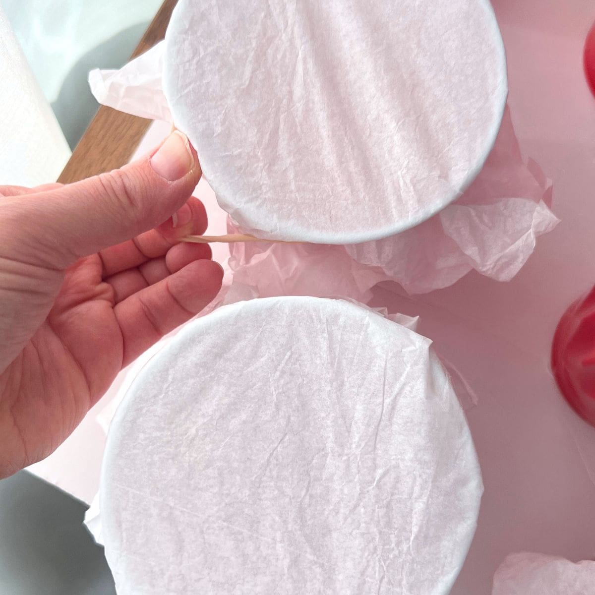 hand pulling rubber band around tissue paper covered plastic cup.