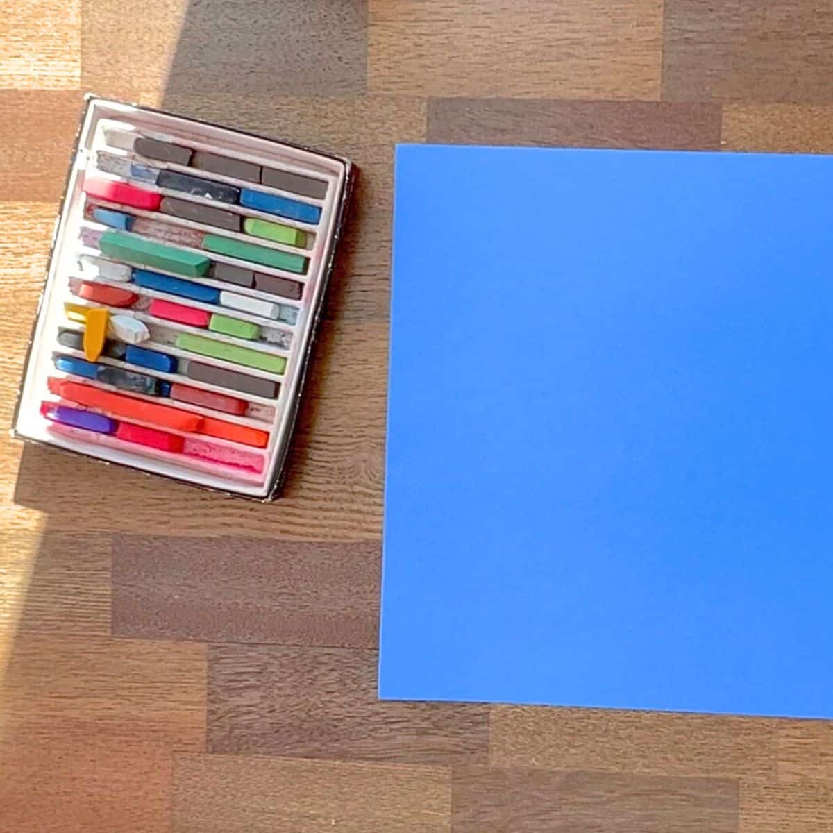 chalk pastels and blue construction paper on a table.