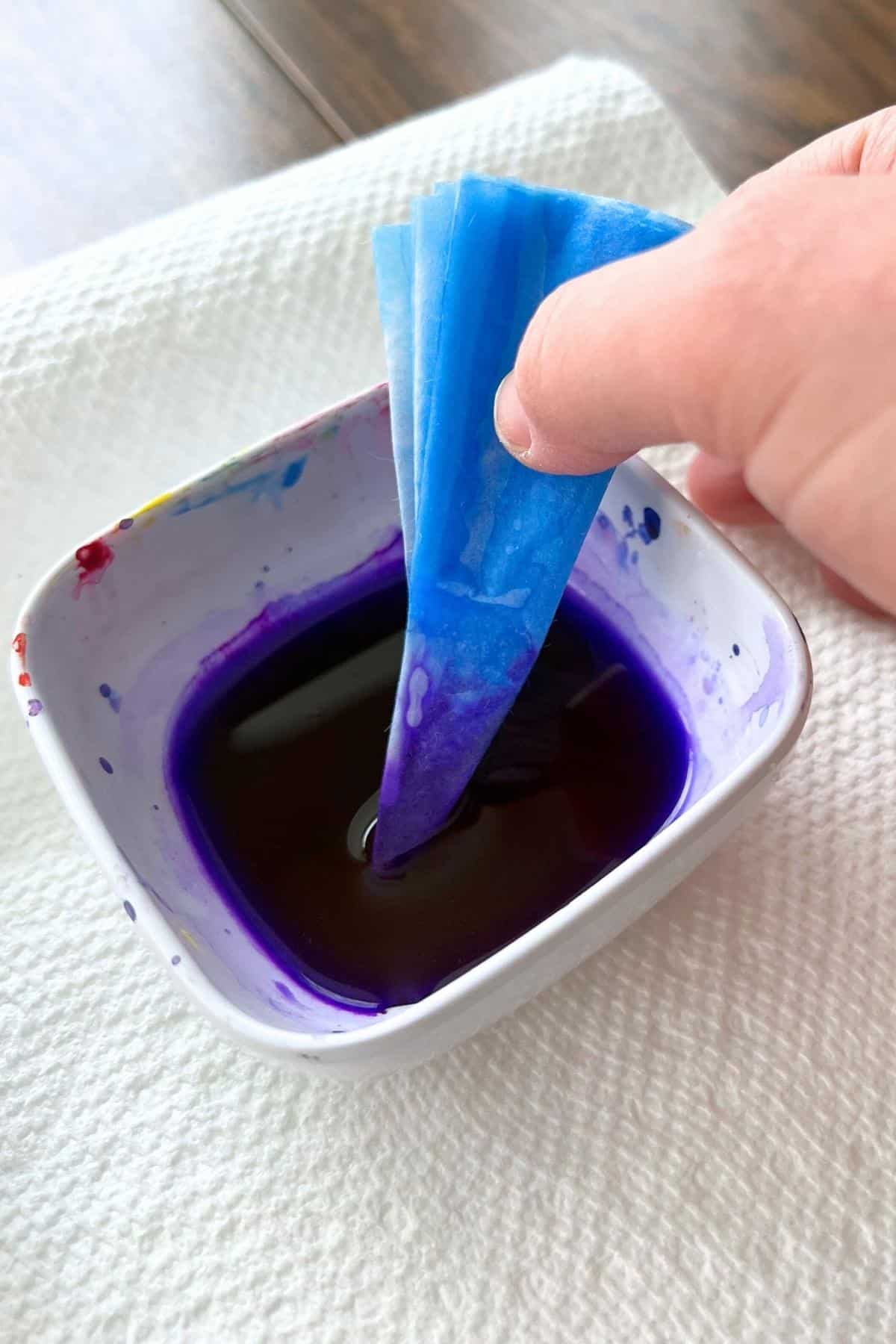 hand holding folded coffee filter and dipping in purple liquid paint.