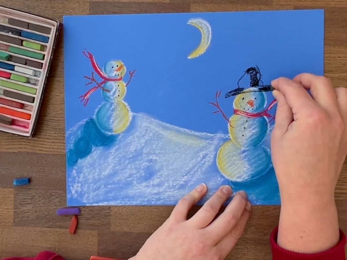 hand adding snowman's hat to chalk drawing.