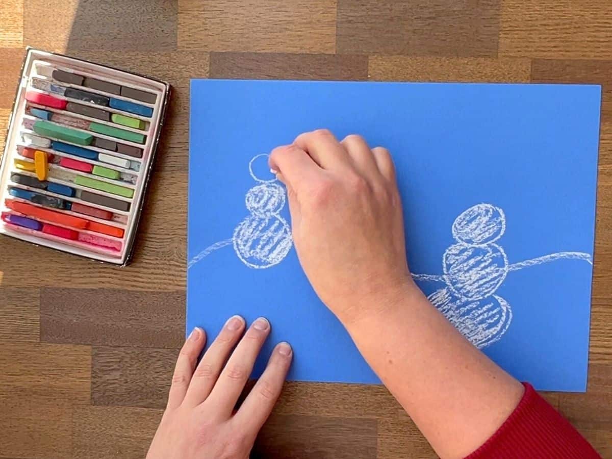 hand coloring white chalk pastel inside snowmen drawing.