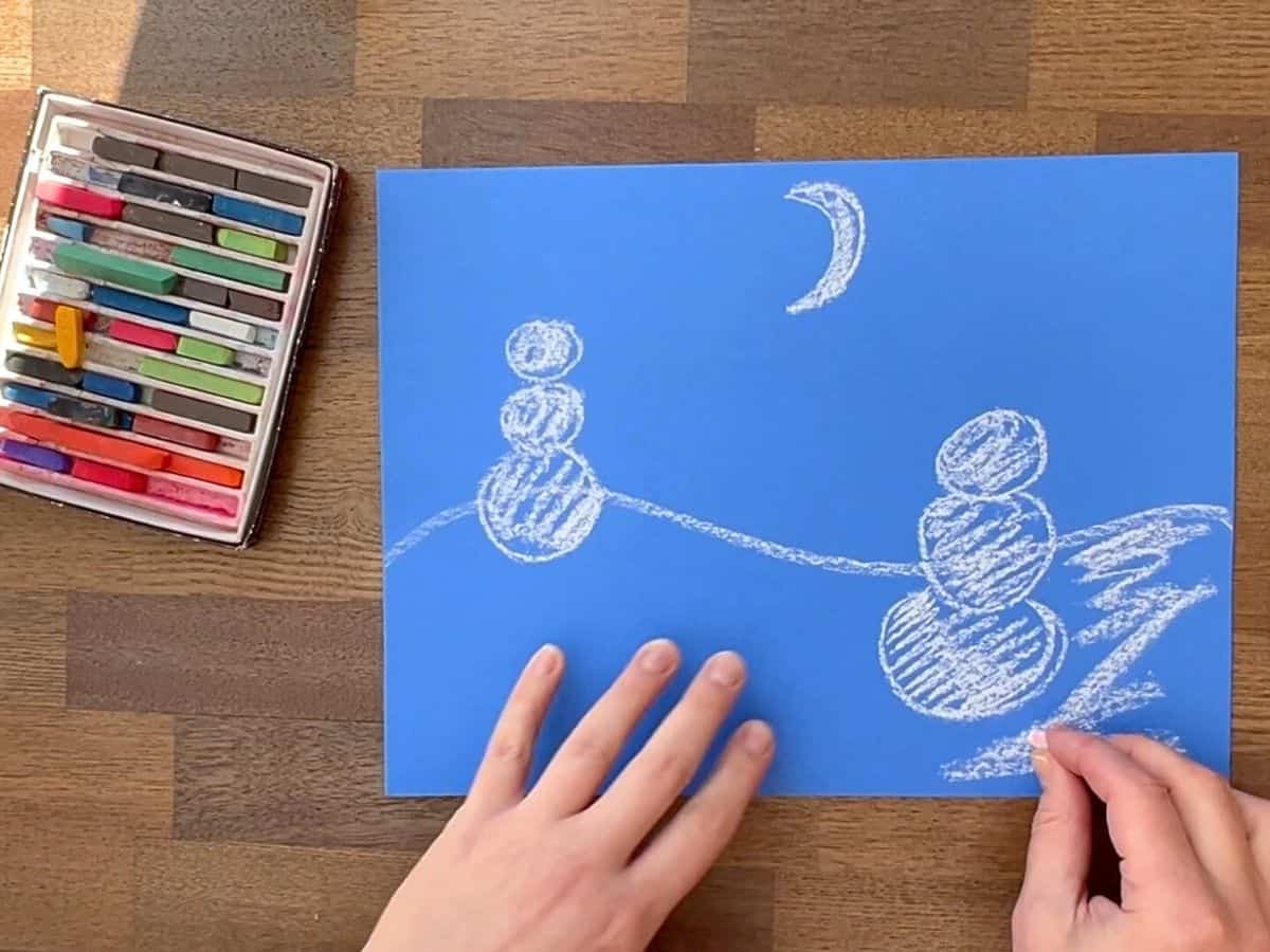 hand adding more chalk pastel to snowman drawing.