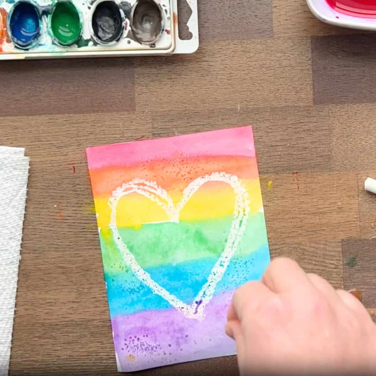 hand adding salt to a rainbow heart painting.