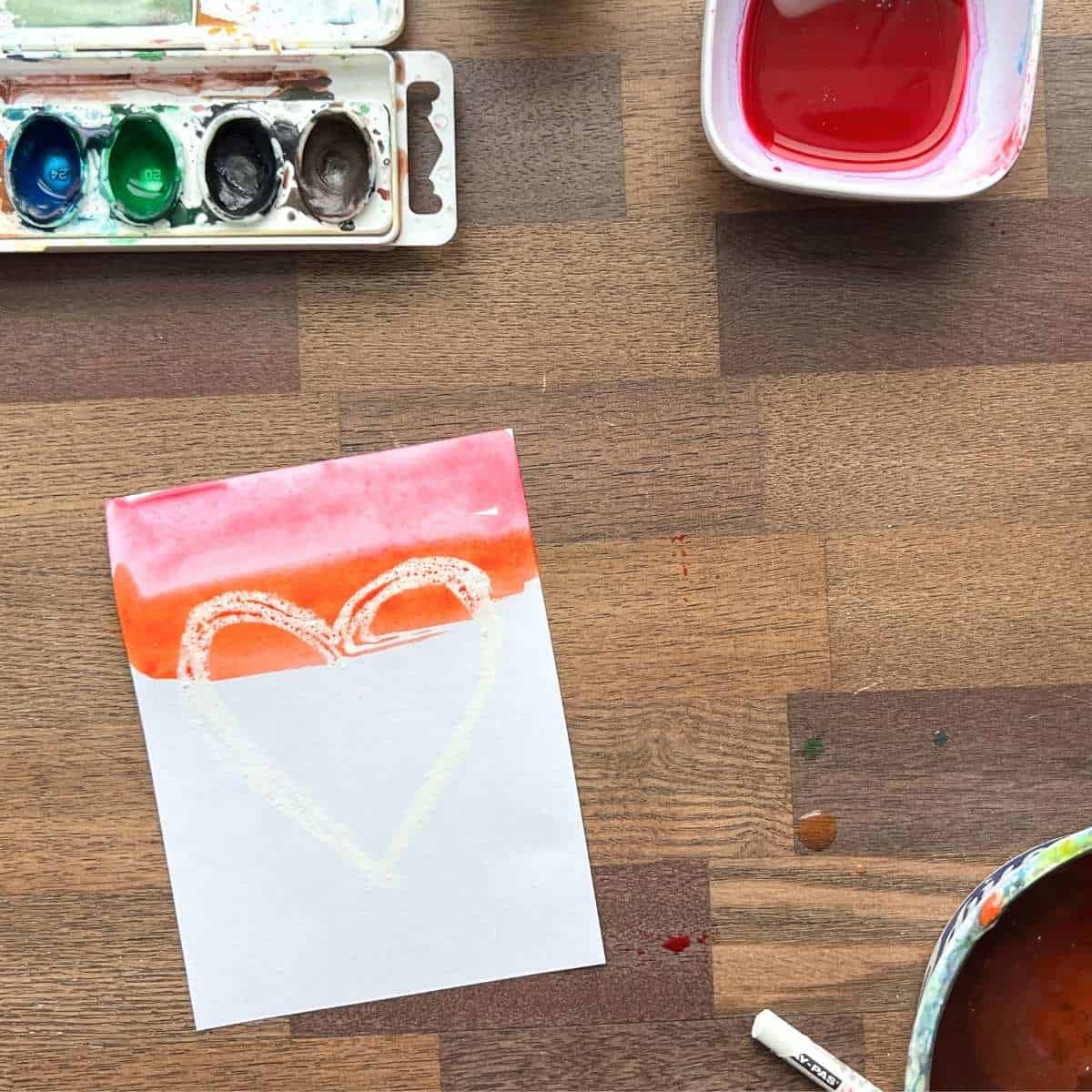red and orange watercolor paint on top of white drawn heart on paper.