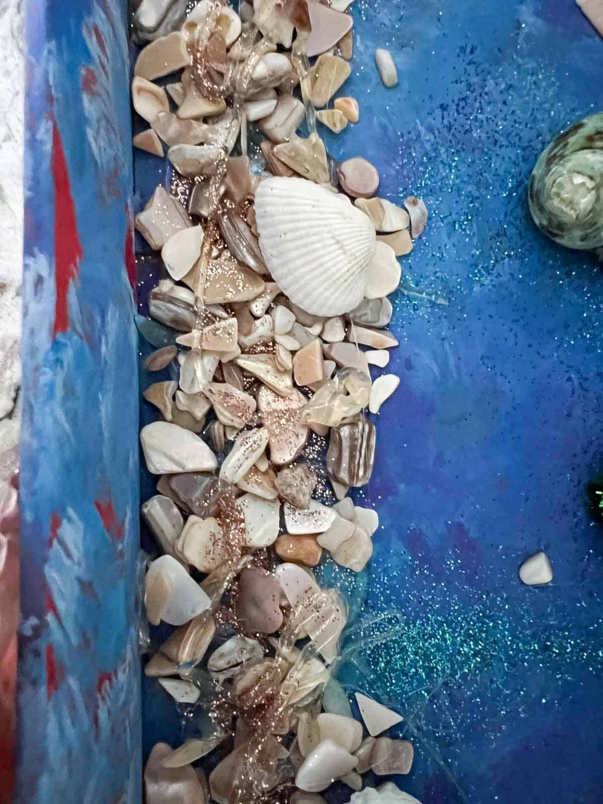 small rocks, seashells and glitter in shoebox.
