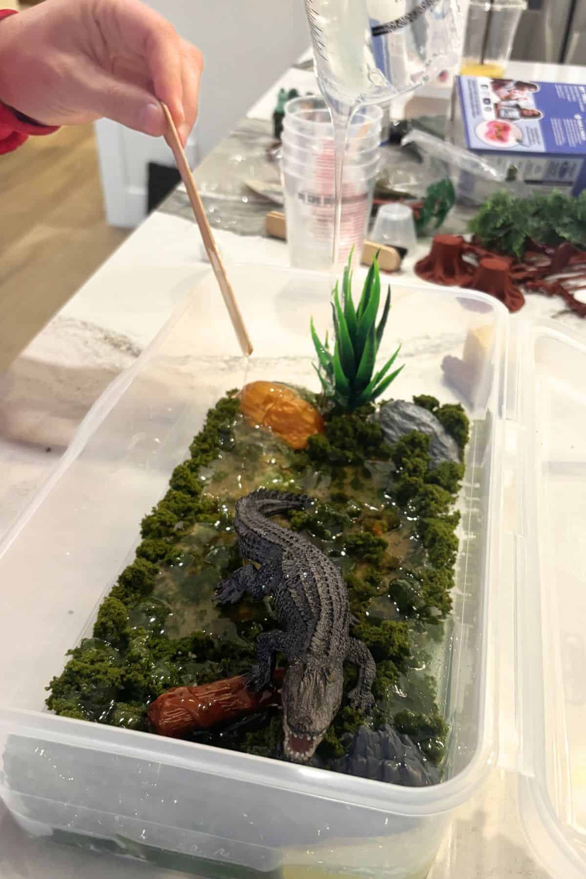 hand pouring resin on top of crocodile habitat.