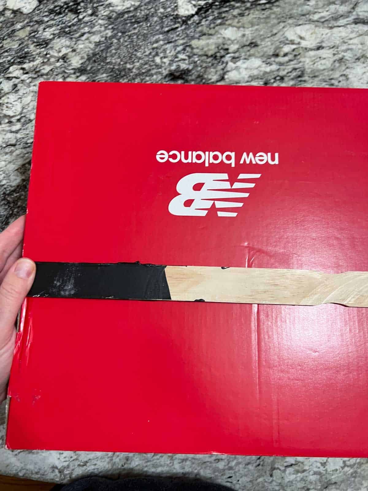 hand holding old wooden paint stick on red shoebox.