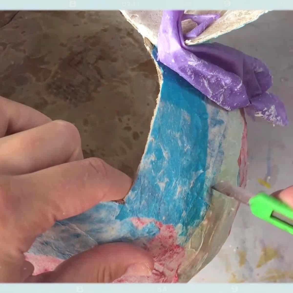 hand holding xacto knife cutting a hole.