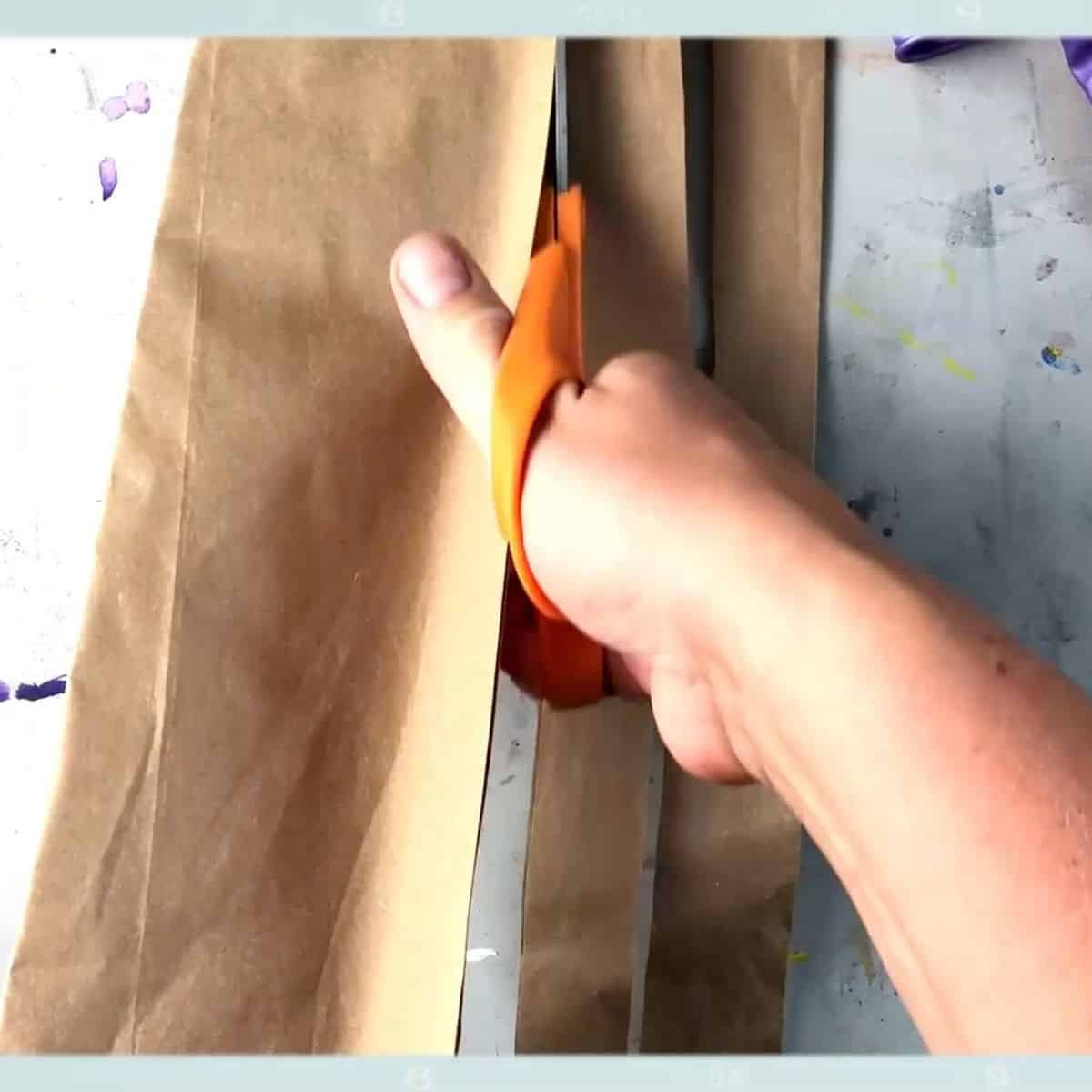 hand with scissors cutting strips of brown bag.