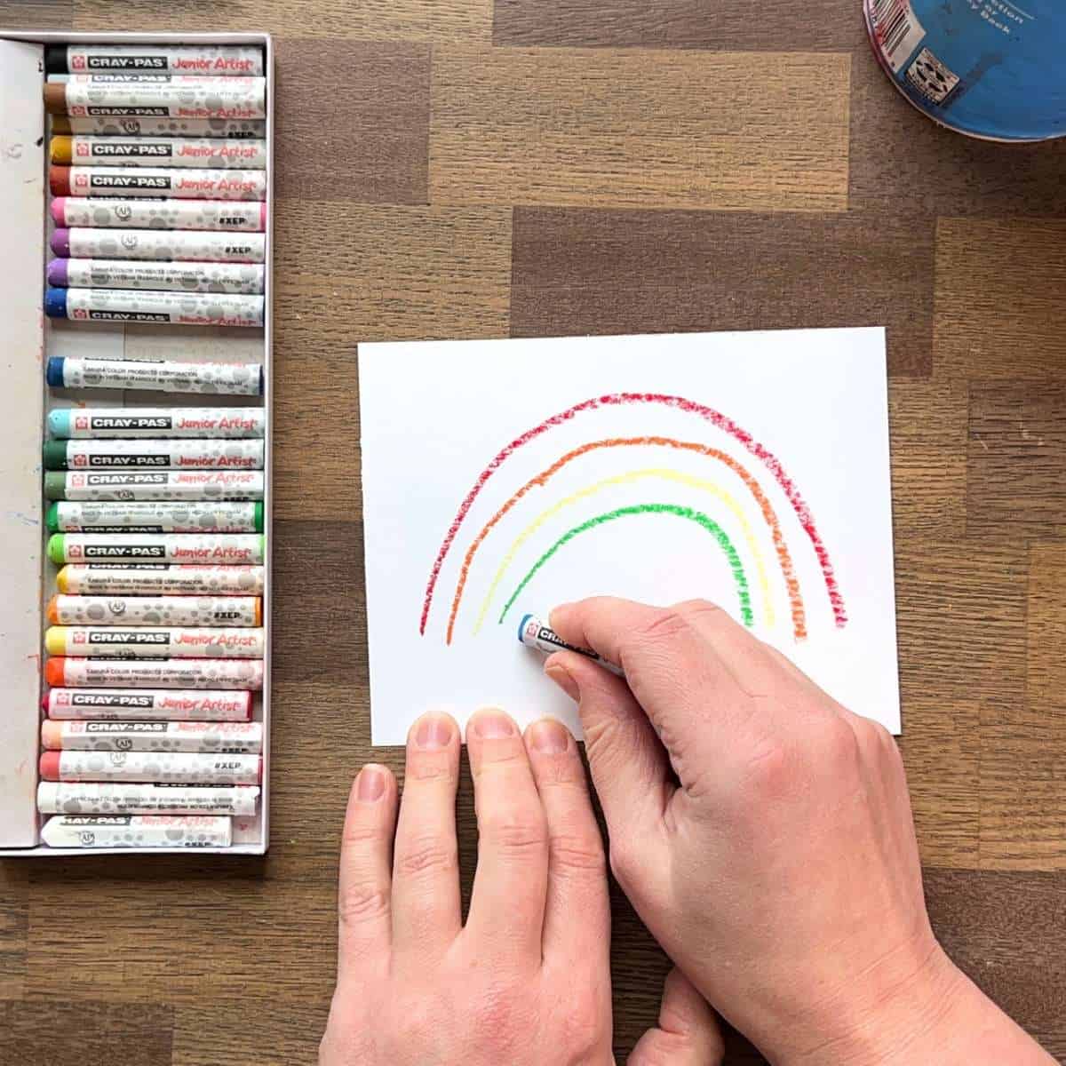 hand drawing a rainbow on white paper with oil pastels.