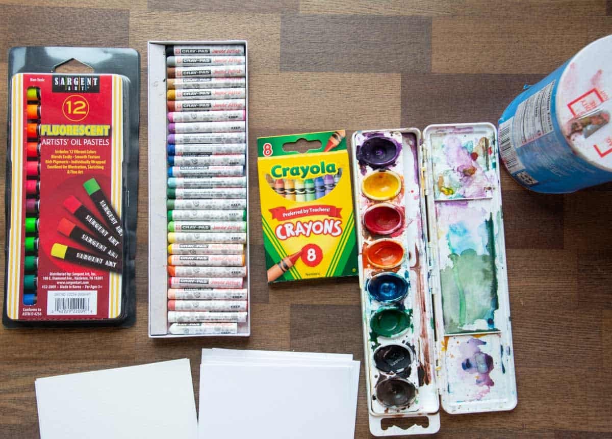 watercolor paints, salt, oil pastels and crayons on a table.
