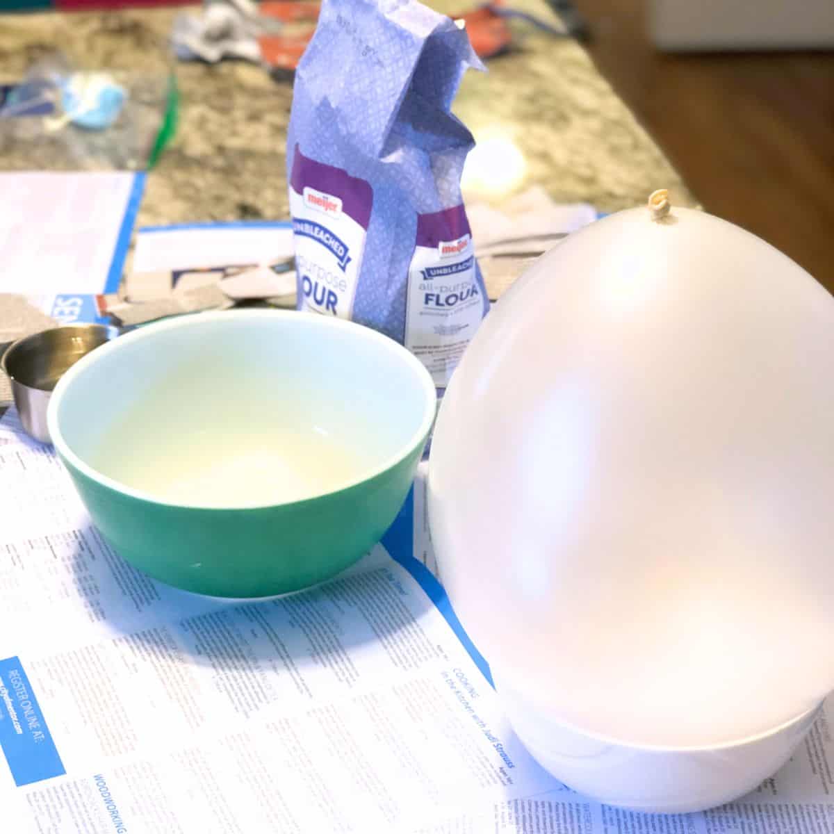 balloon, newspaper, bowl, flour and measuring cup on a countertop.