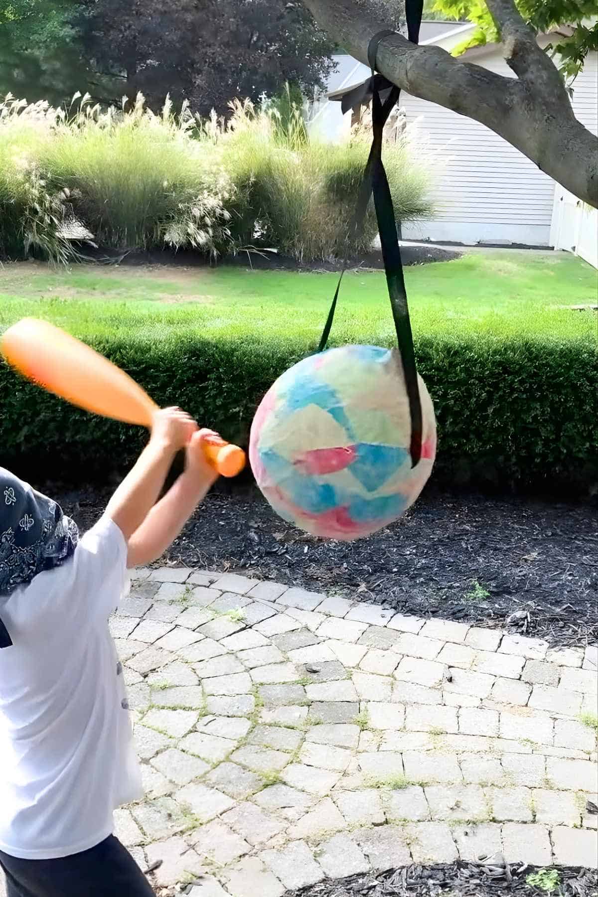 little boy hitting balloon piñata with a plastic bat.