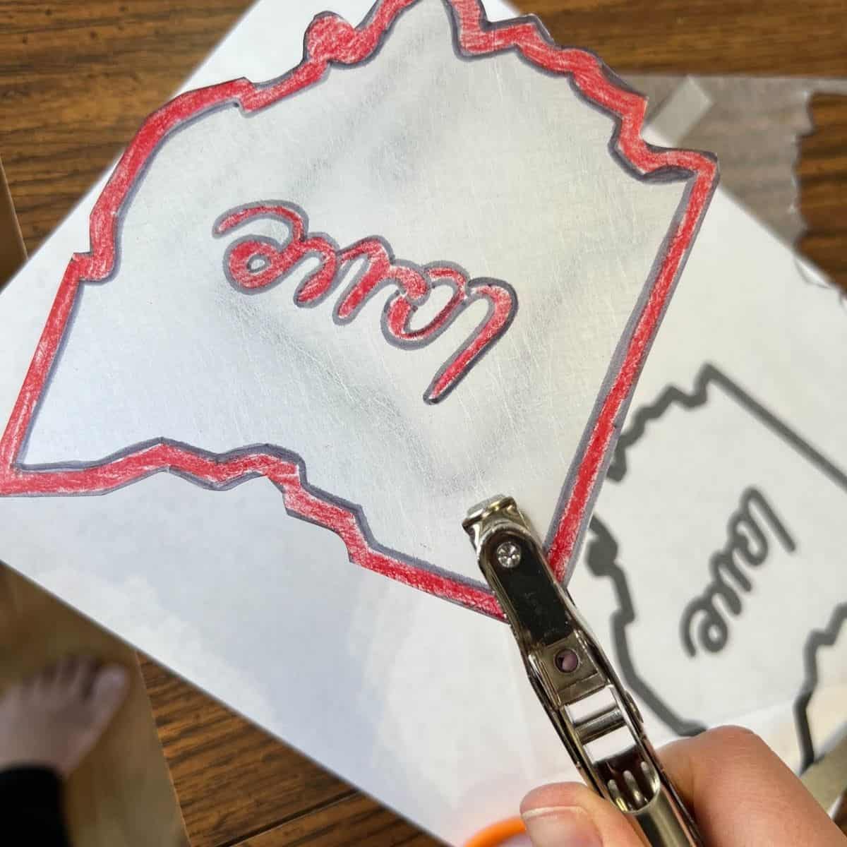 hand holding hole punch and piece of colored shrink plastic.