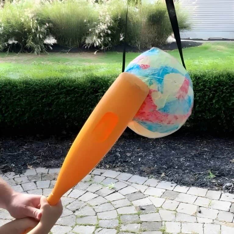 yellow plastic bat hitting balloon piñata hanging from a tree.