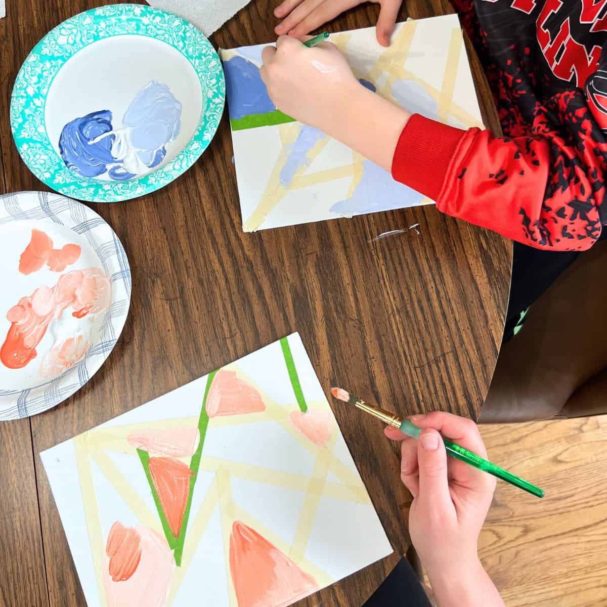 hands holding paintbrushes painting light colors on your canvas board.
