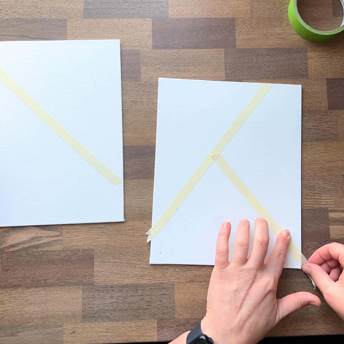 hands taping diagonal lines on canvas boards.