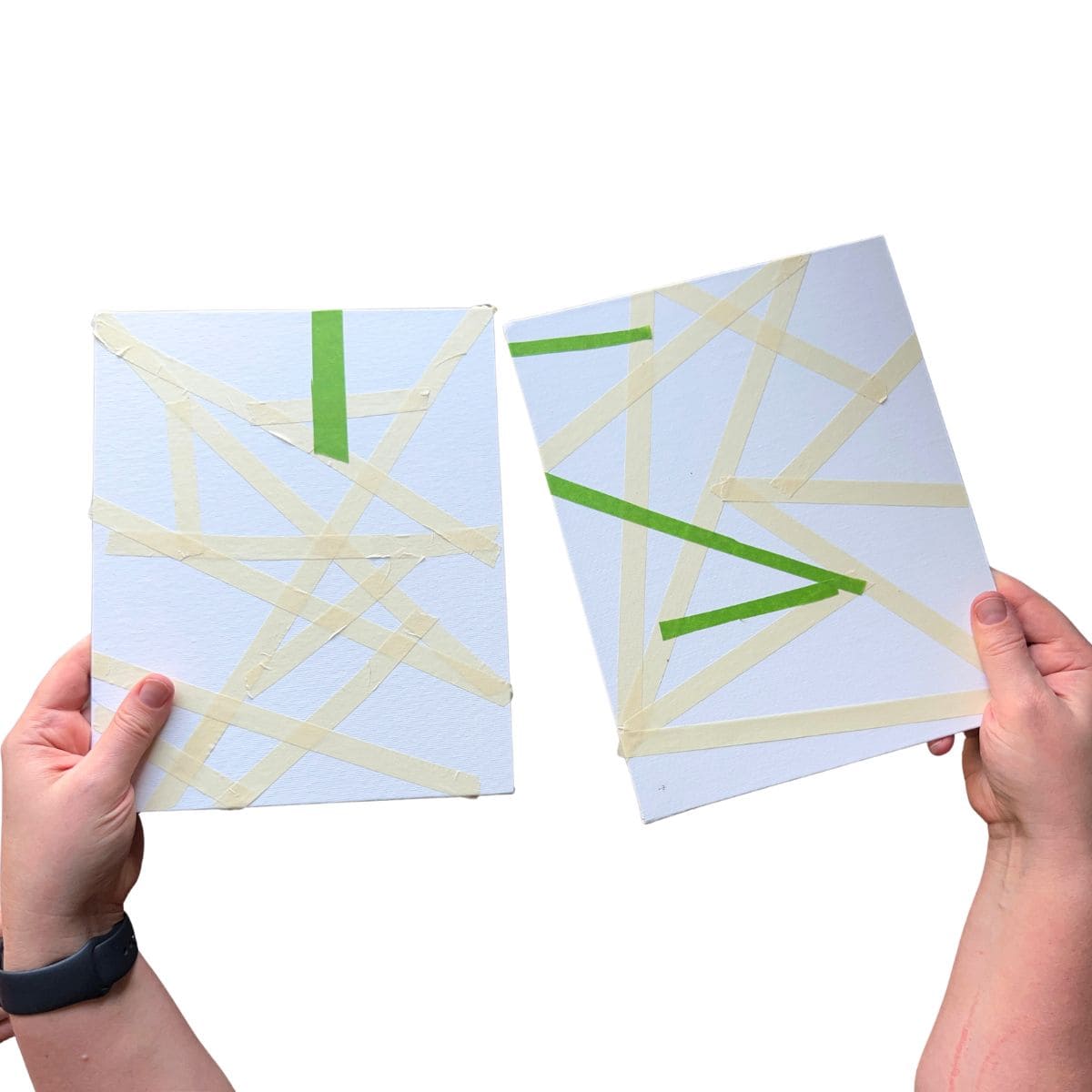 hands holding taped designs on canvas boards.
