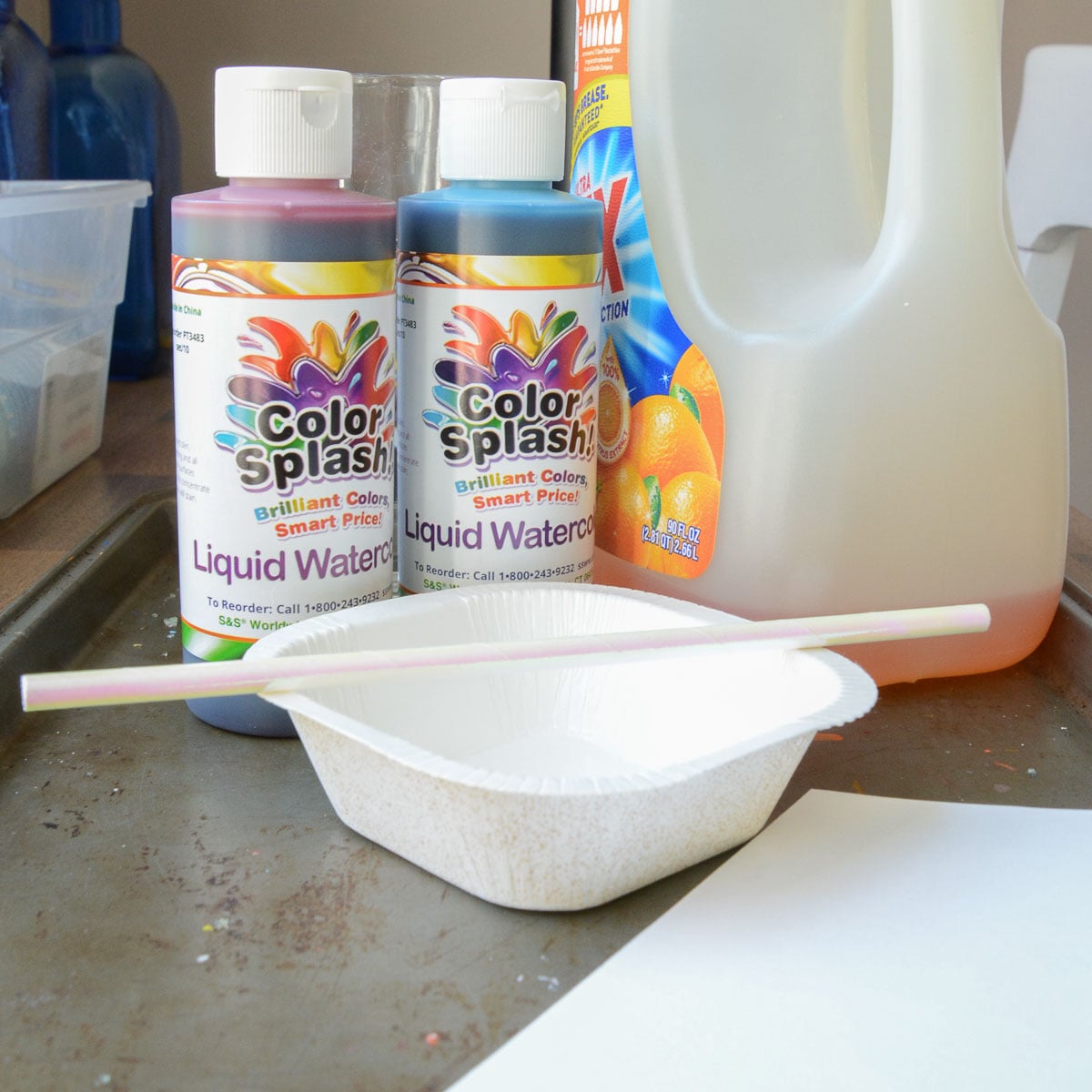 liquid watercolor paints, straw, container and dish soap on a cookie sheet.