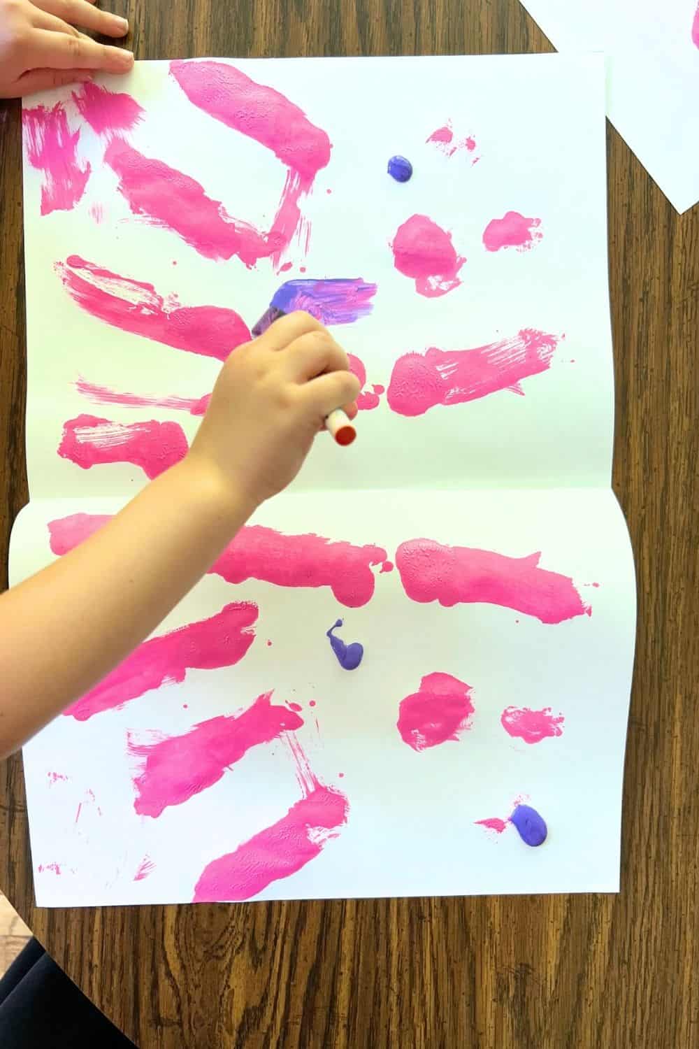 child hand holding a foam brush and adding paint to white paper.