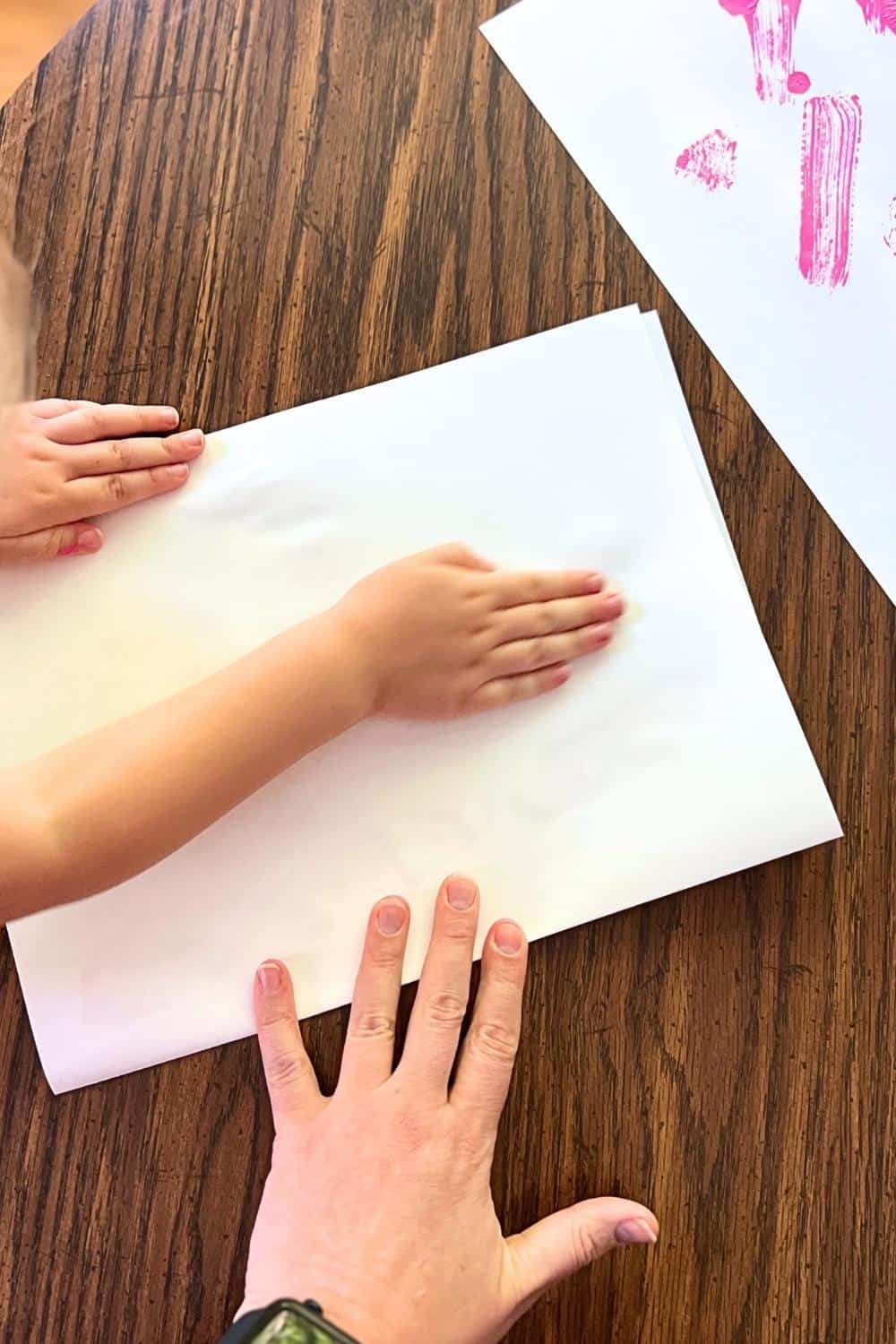 child and adult hand rubbing the folded white paper.