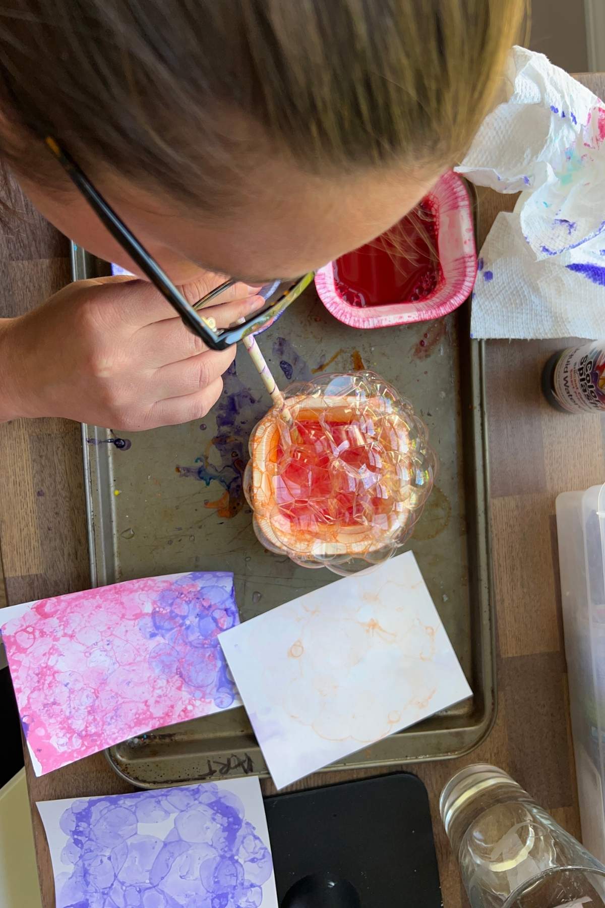 woman in glasses blowing bubbles in paint mixture.