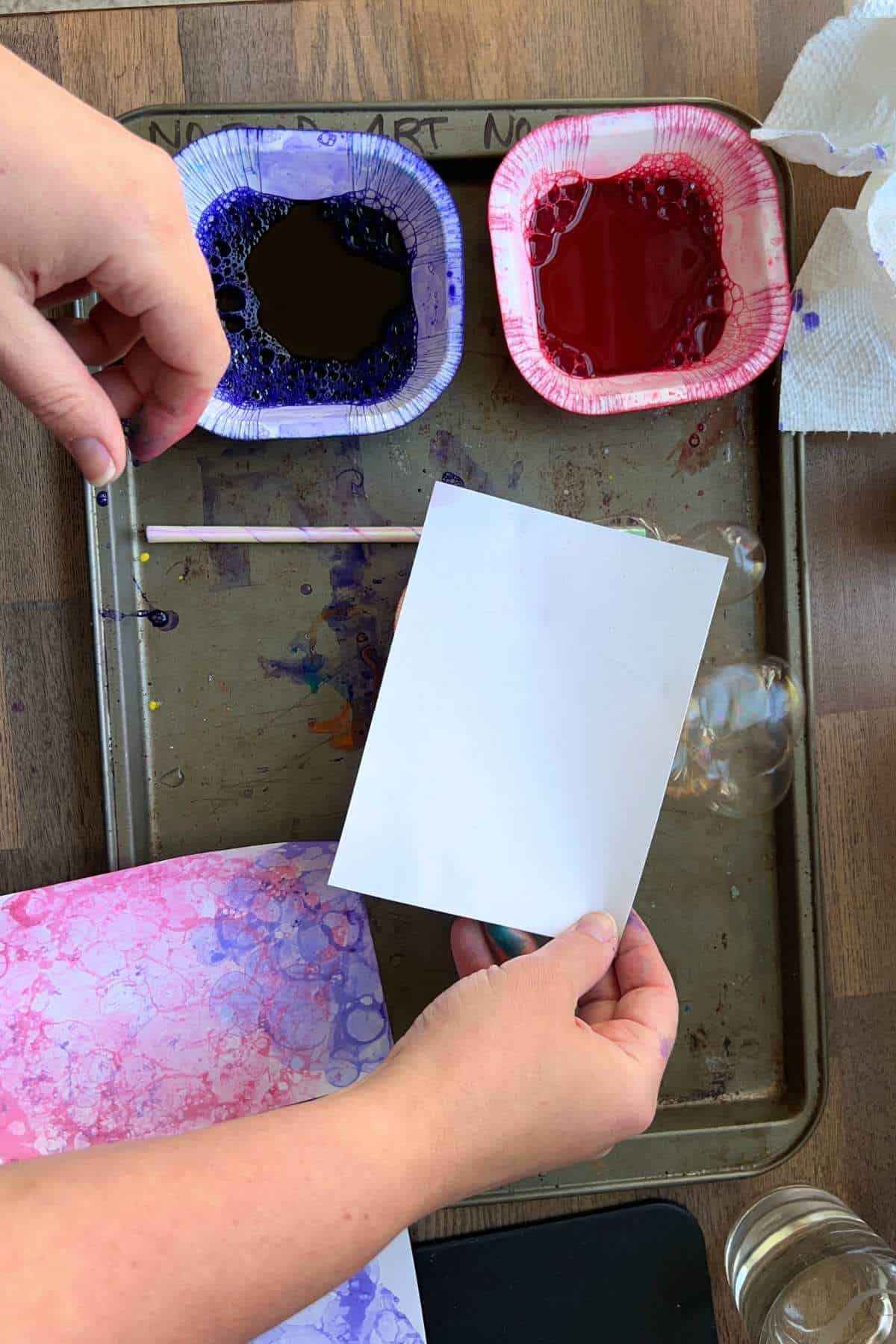 small white paper on top being pressed on container of paint on a tray.