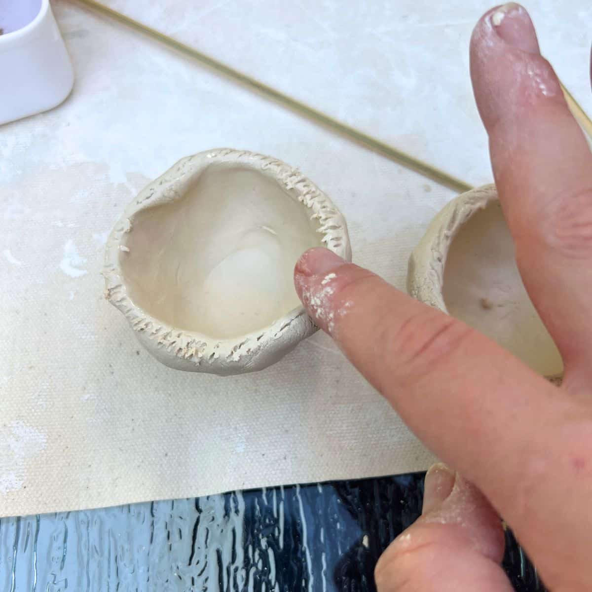 one finger adding water to edge of clay pinch pot.