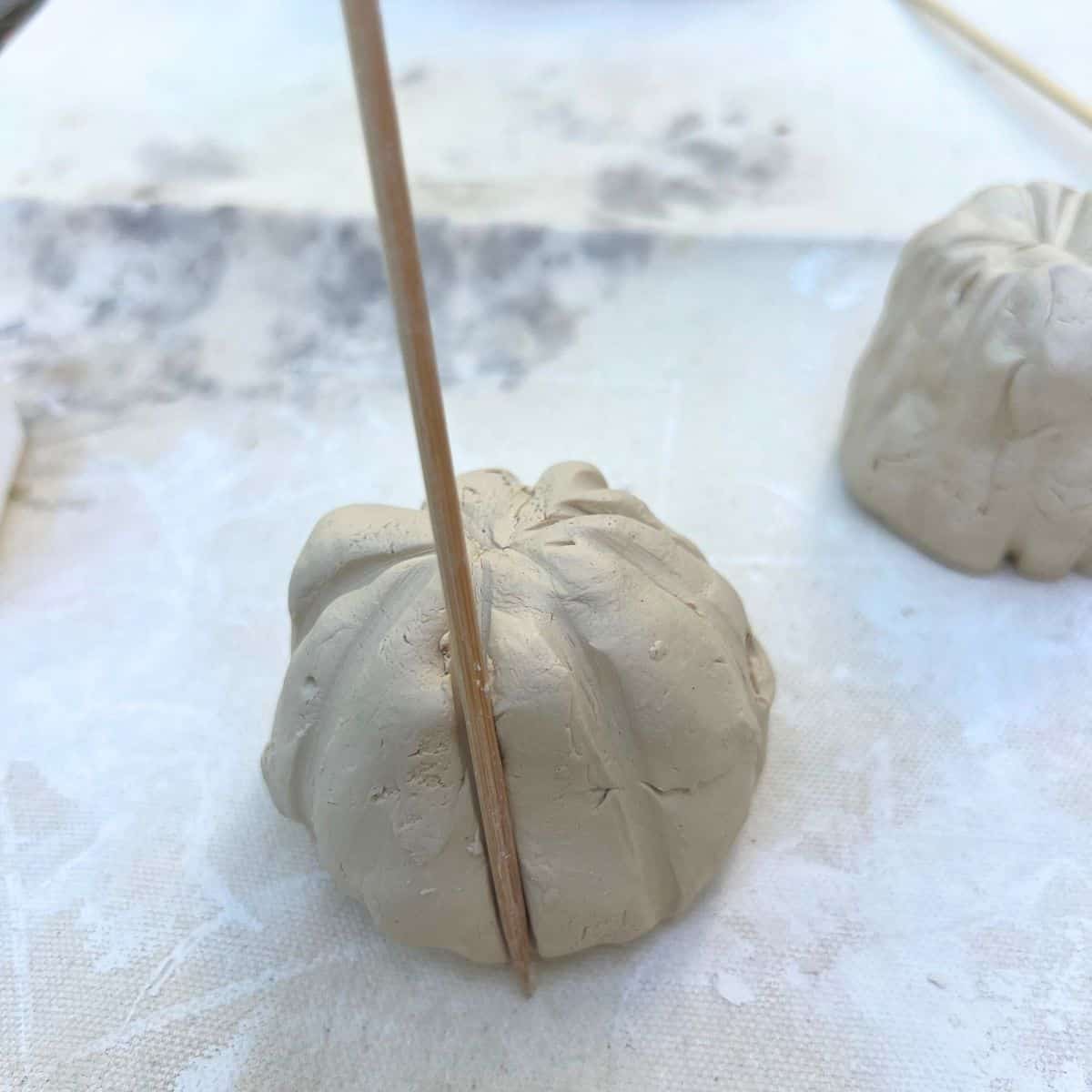 wooden skewer pressing ridges into clay pumpkin.
