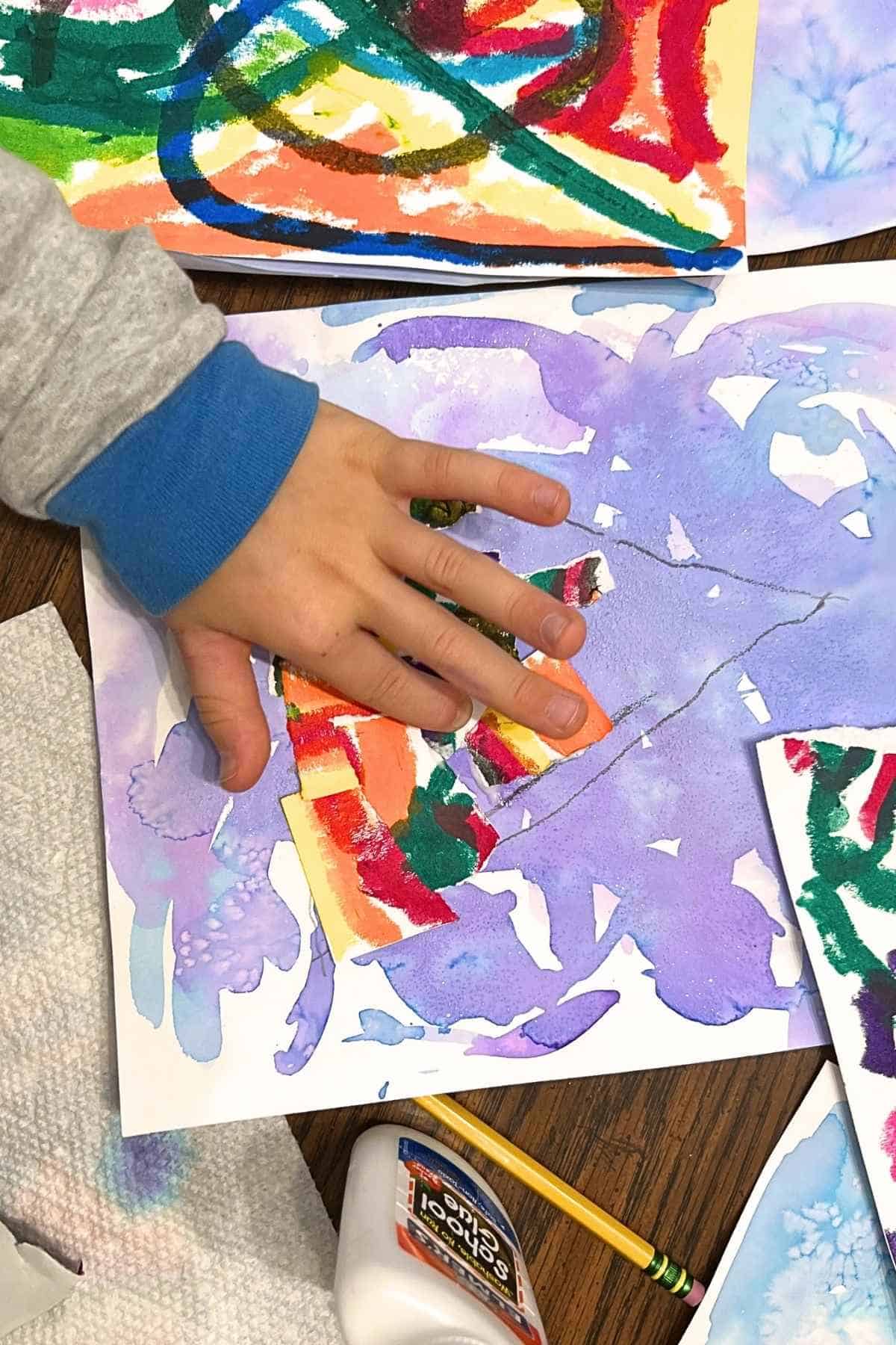 child's hand adding colorful paper to painted paper.
