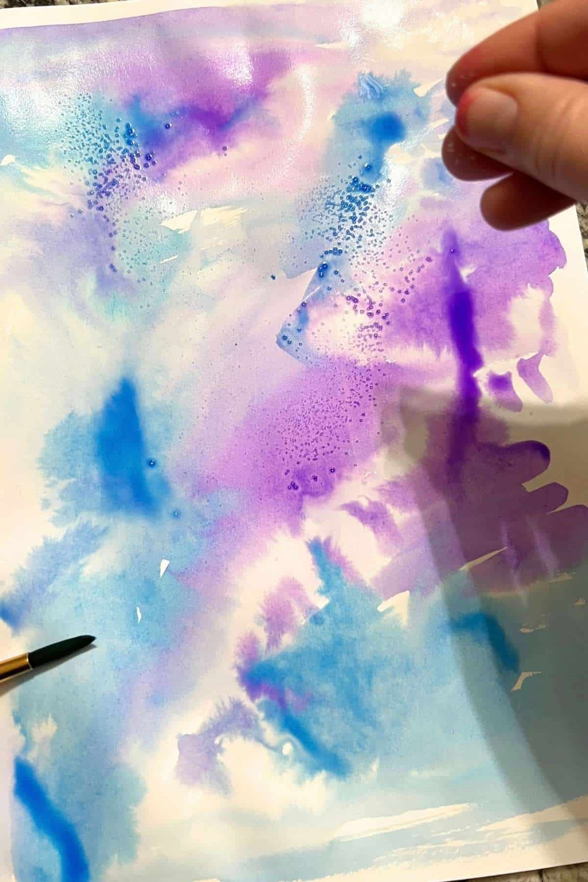 hand adding salt to watercolor paint on a paper.