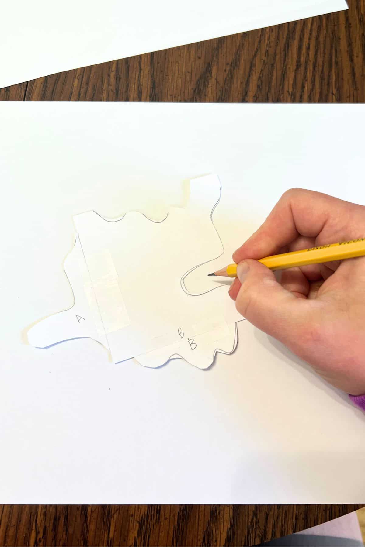 hand holding pencil and tracing around paper shape.